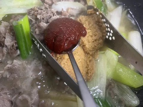 Doenjang, gochujang, and gochugaru simmering with beef broth in a pot